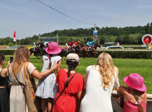 Rennbahnbesucher betrachten die Pferde und Jockeys im Rennen beim Sparkassen-Renntag